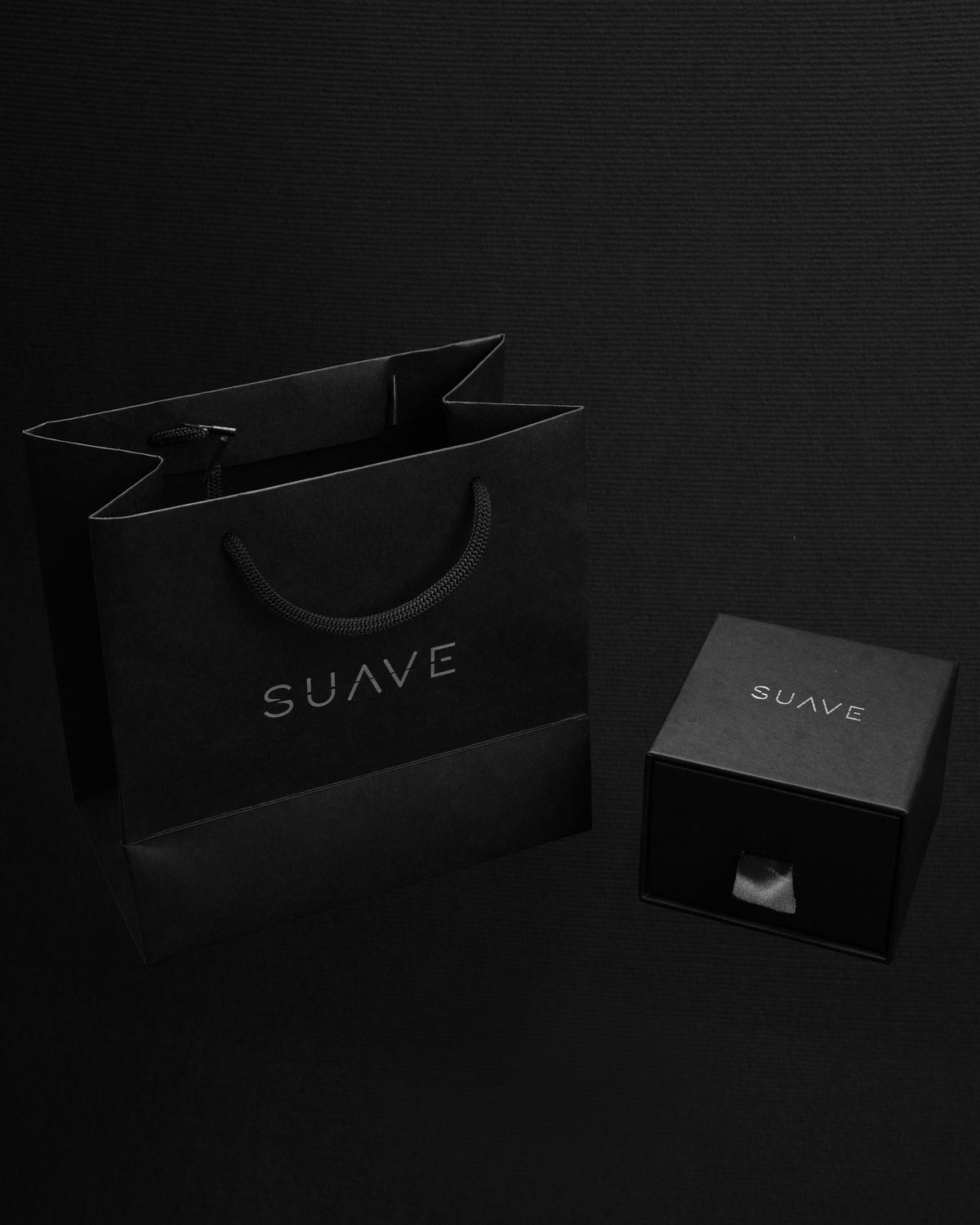 Black 'SUAVE' branded shopping bag and box on a dark background